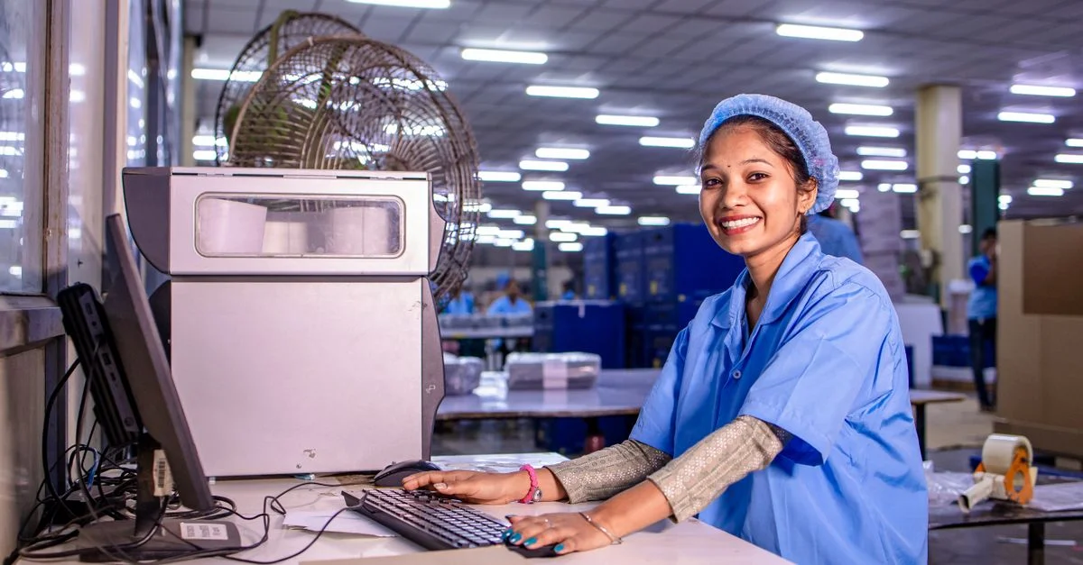 Portrait d'une ouvrière souriante à son bureau dans une usine de production très éclairée.