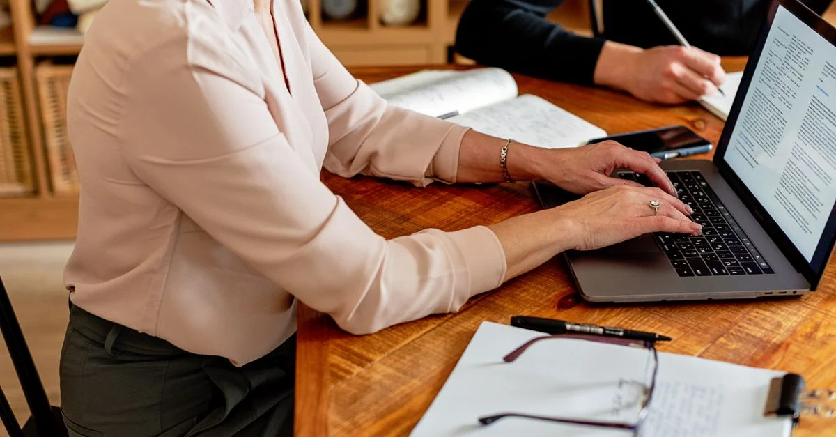 Deux professionnels à un bureau, utilisant un ordinateur portable et prenant des notes dans un environnement de travail collaboratif.