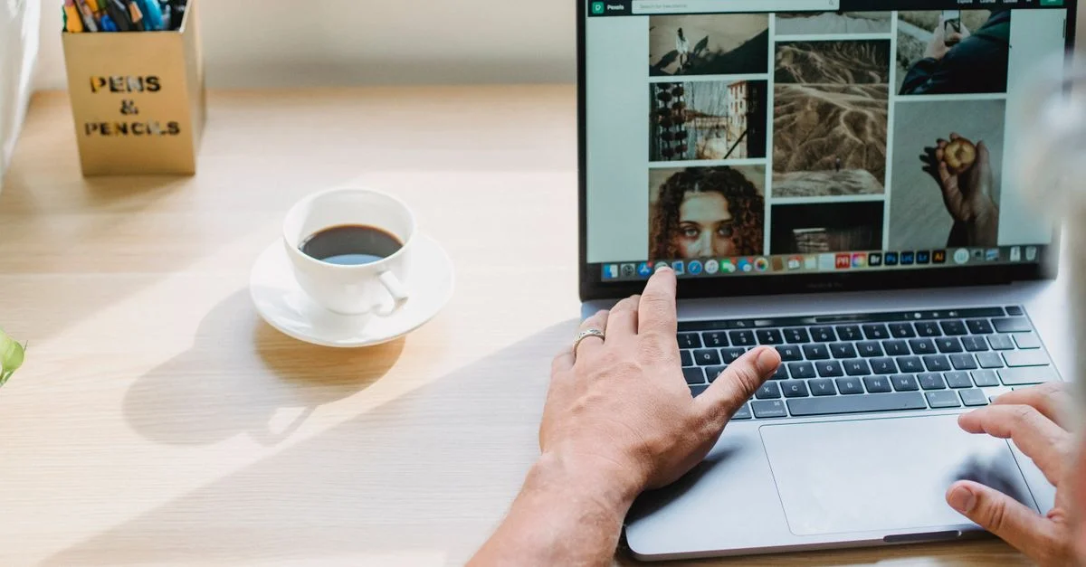 Un homme naviguant sur un site web sur un ordinateur portable avec une tasse de café sur un bureau ensoleillé.