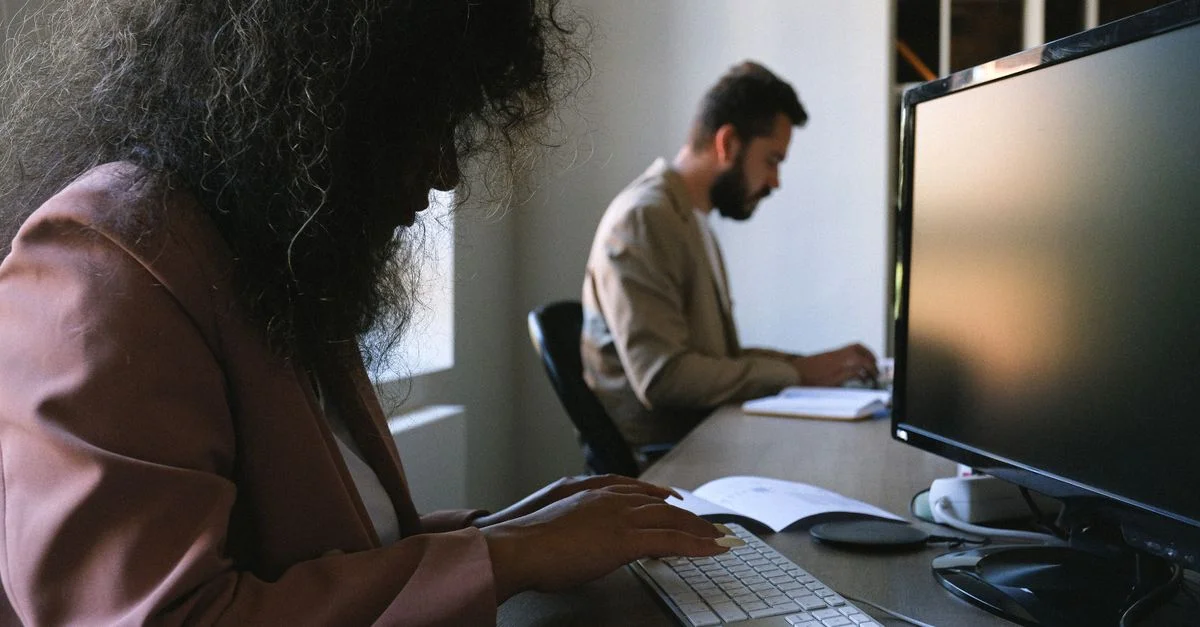 Deux professionnels concentrés sur leur travail dans un bureau moderne, utilisant des ordinateurs et des cahiers.