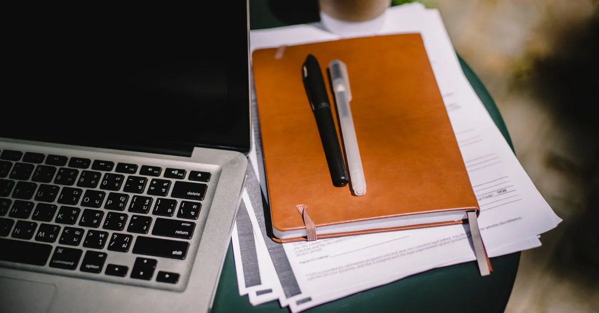 Vue aérienne d'un espace de travail avec un ordinateur portable, un carnet et une tasse de café sur une table extérieure.