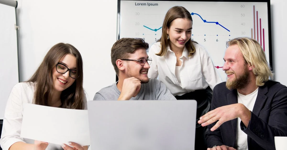 Équipe commerciale participant à une discussion animée dans un bureau moderne avec des graphiques visibles en arrière-plan.