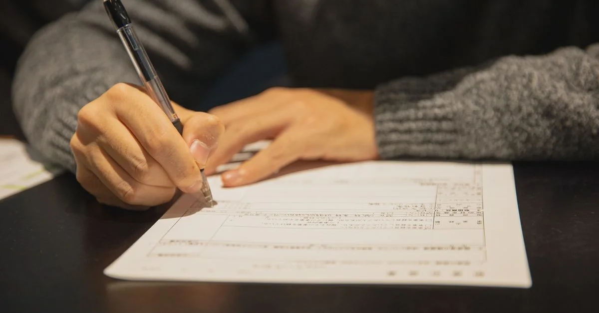 Gros plan d'un homme en pull gris signant un document à un bureau dans un cadre de bureau.