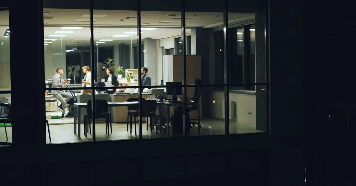 Une réunion de bureau nocturne avec des professionnels travaillant dans un bureau moderne à murs en verre.