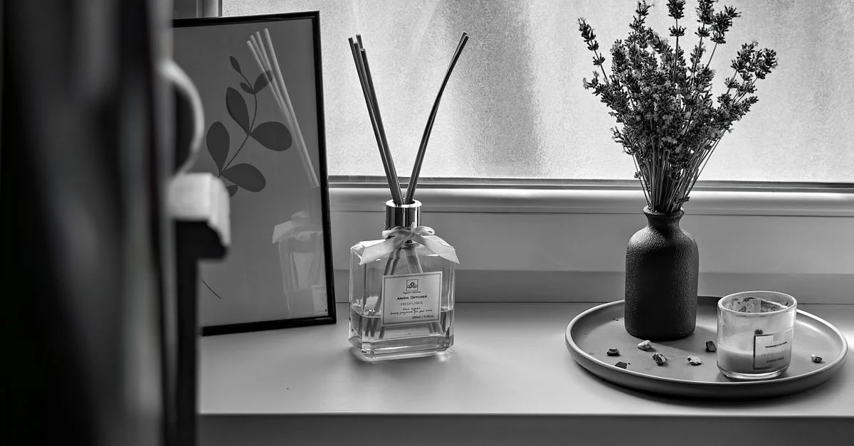Image en noir et blanc d'un rebord de fenêtre avec diffuseur de parfum, lavande et bougie.