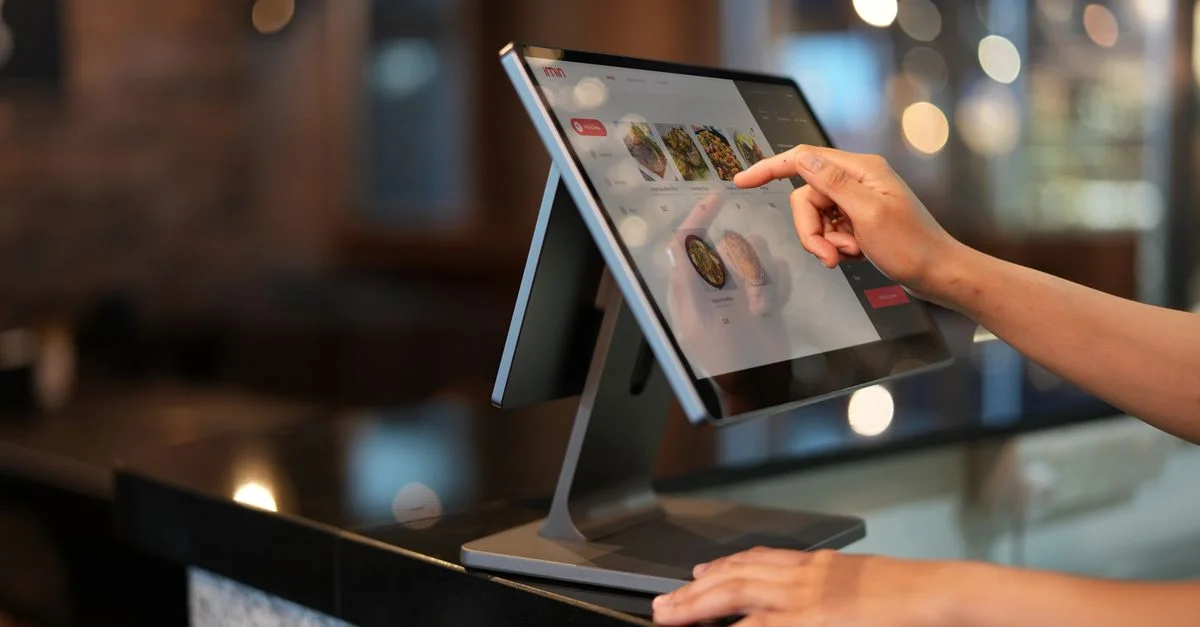 Gros plan d'une main interagissant avec un système POS à écran tactile dans un cadre de restaurant.